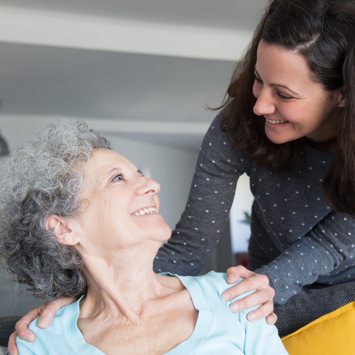 Eldery woman and her daughter looking each other in the eyes and smiling