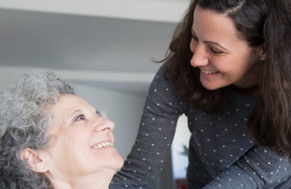 Eldery woman and her daughter looking each other in the eyes and smiling